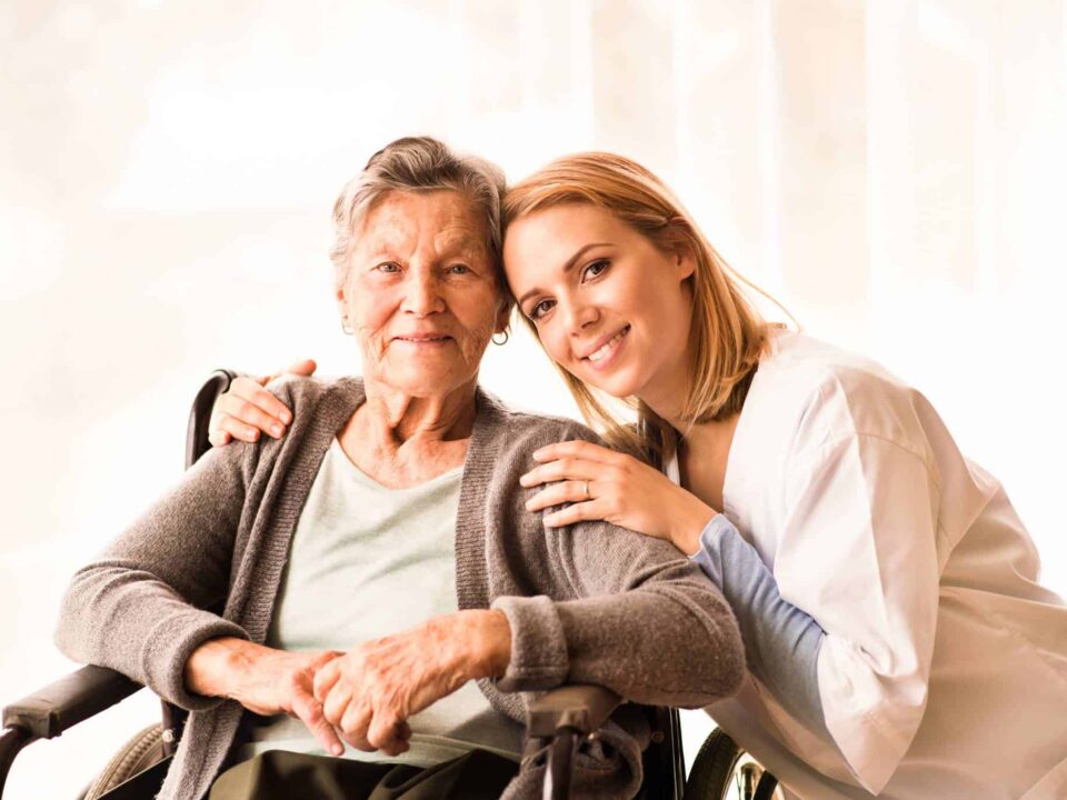 a female caregiver hugging a senior woman on wheelchair